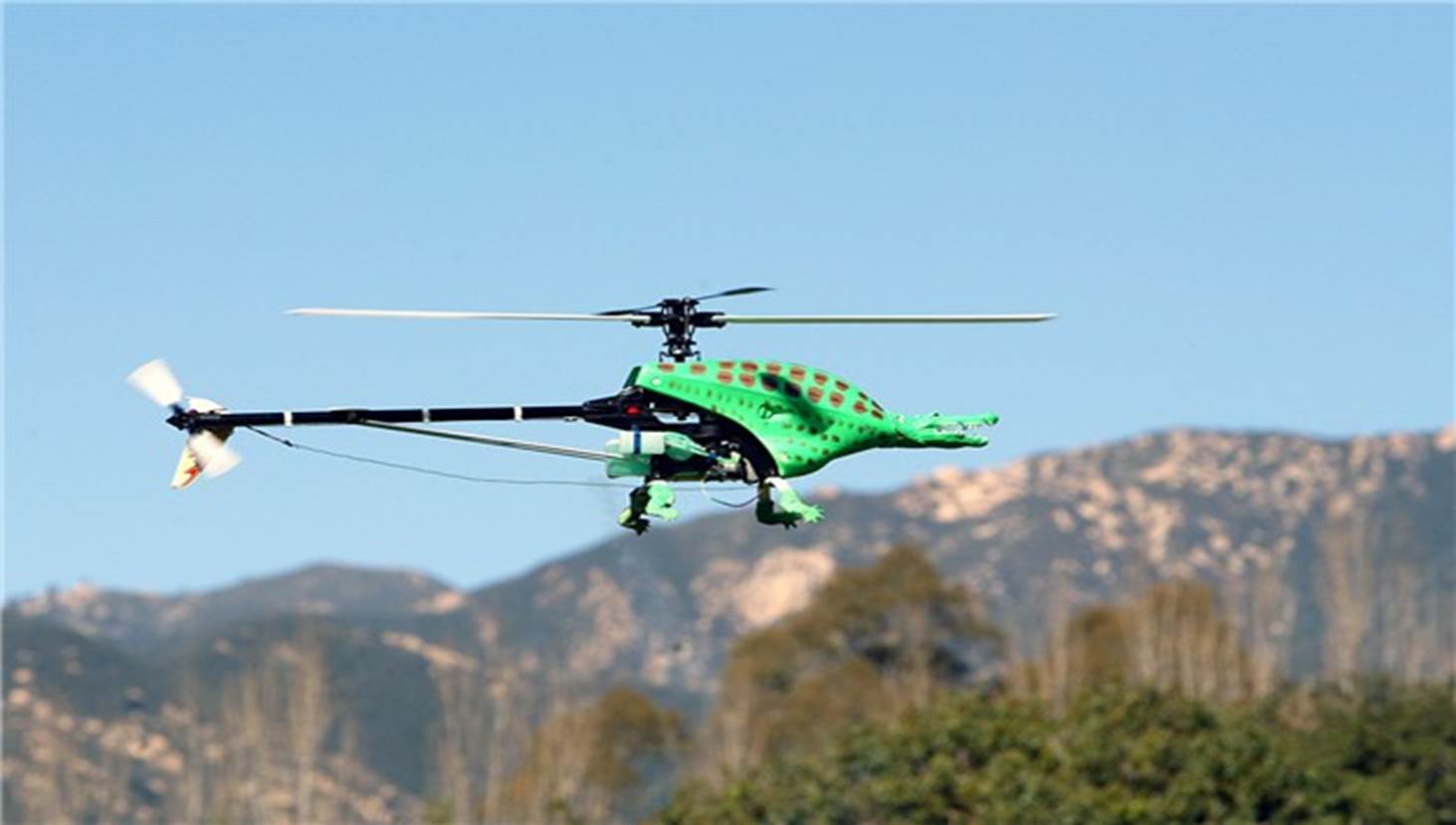 A green helicopter flying in the air
Description automatically generated